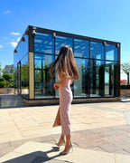 Rochie roz pudrat mulata pe corp roz cu slit, fără mâneci, în fața unui clădiri moderne de sticlă.