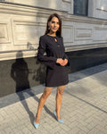 Rochie neagra scurtă cu franjuri din cristale și mâneci lungi, în fundal urban.