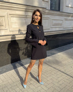 Rochie neagra scurtă cu franjuri din cristale și mâneci lungi, în fundal urban.