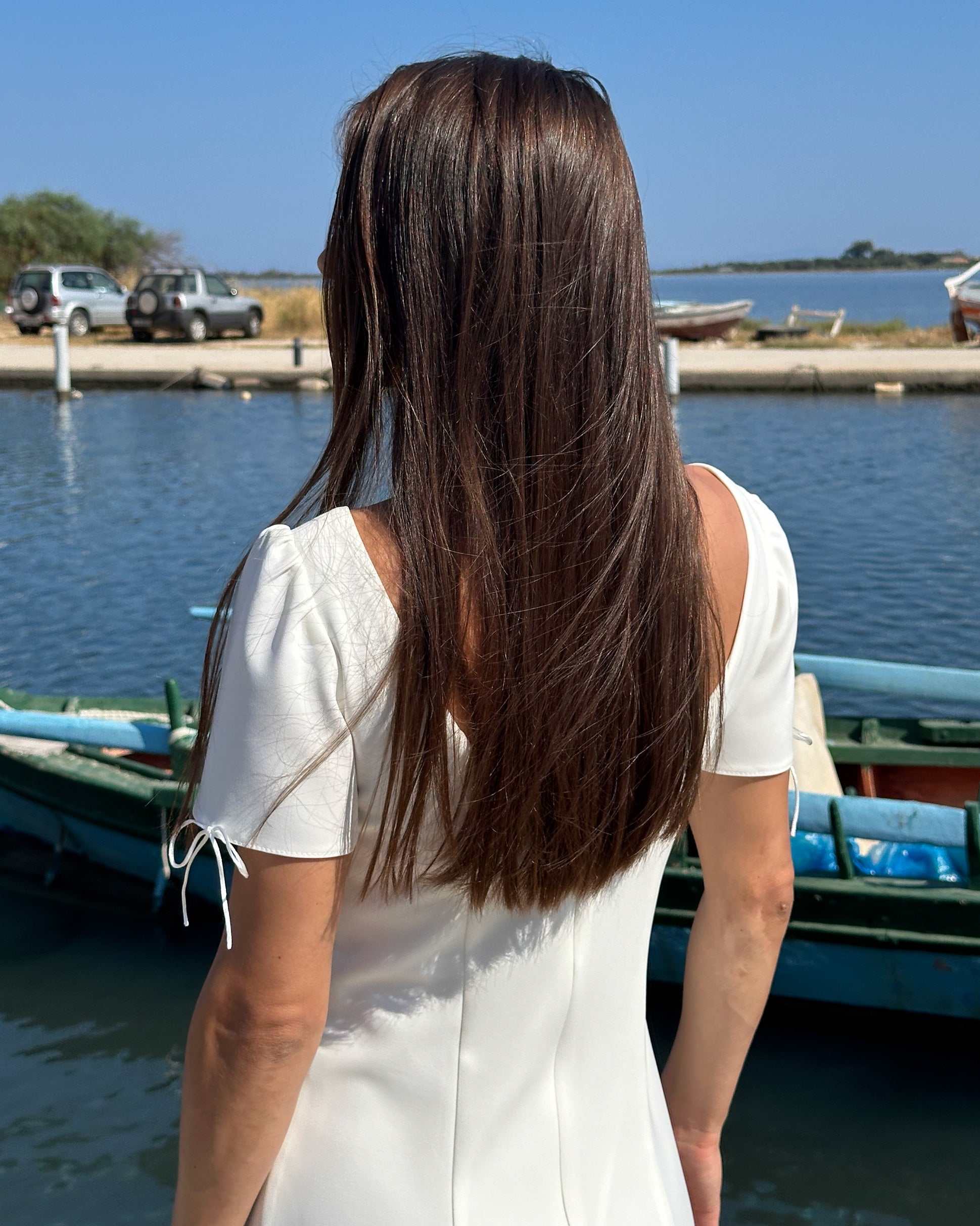 Rochie albă scurtă cloș cu mâneci, elegantă și feminină, lângă apă.